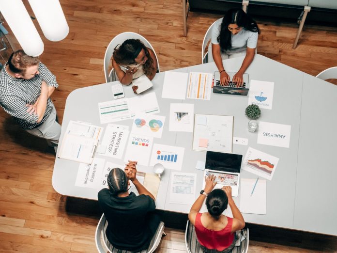 Team collaborating on a PowerPoint presentation around a conference table with charts and business documents